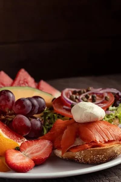 A fresh breakfast plate featuring a smoked salmon bagel, capers, and a vibrant fruit medley.