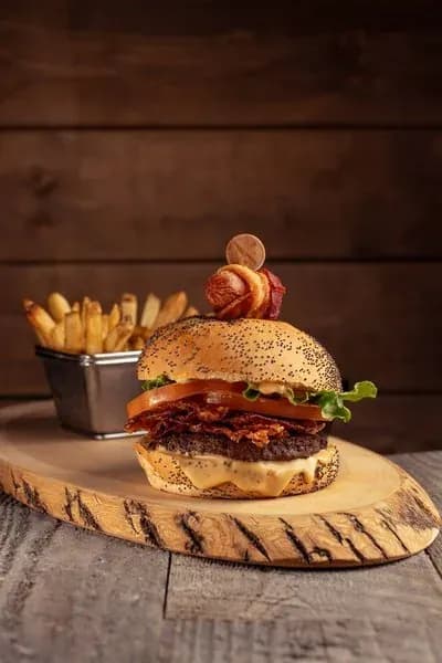 Gourmet bacon cheeseburger served on a rustic wooden board with a side of french fries.